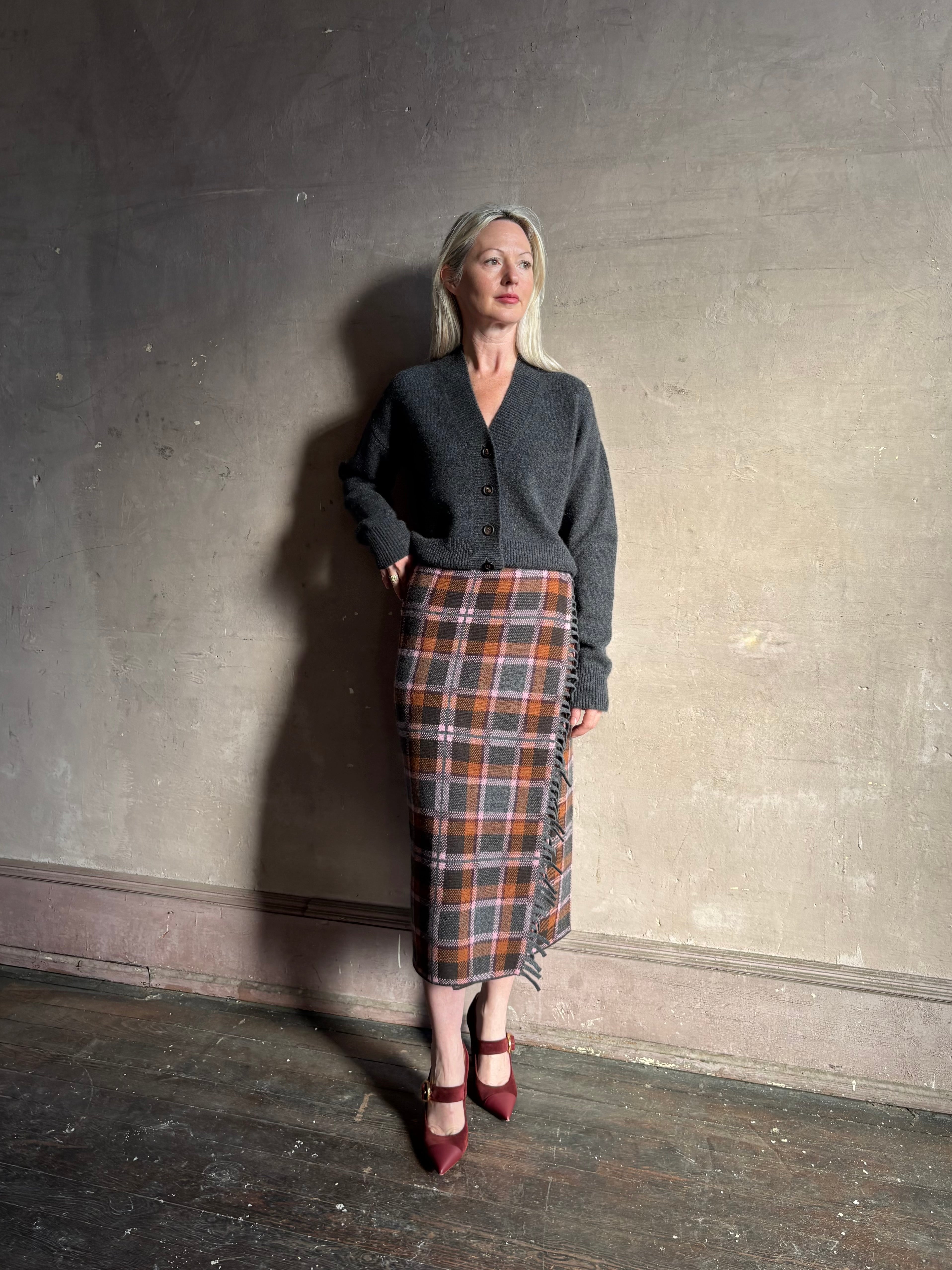 Mature woman wearing a dark gray brown and orange plaid wrap pencil skirt trimmed with fringe by Guest in Residence