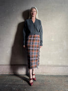 Image of a mature woman wearing a dark gray button-up cardigan styled with Gigi Hadid Guest in Residence grey, brown and orange plaid midi skirt with fringe detailing