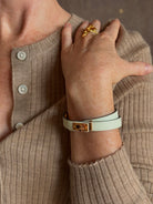 Mature woman wearing Hermès' Mini Kelly Double Tour Wrap Bracelet in Vert d'Eau & Rose Gold pristine, never-worn leather with the iconic Kelly turn-lock. Rare, collectible French luxury