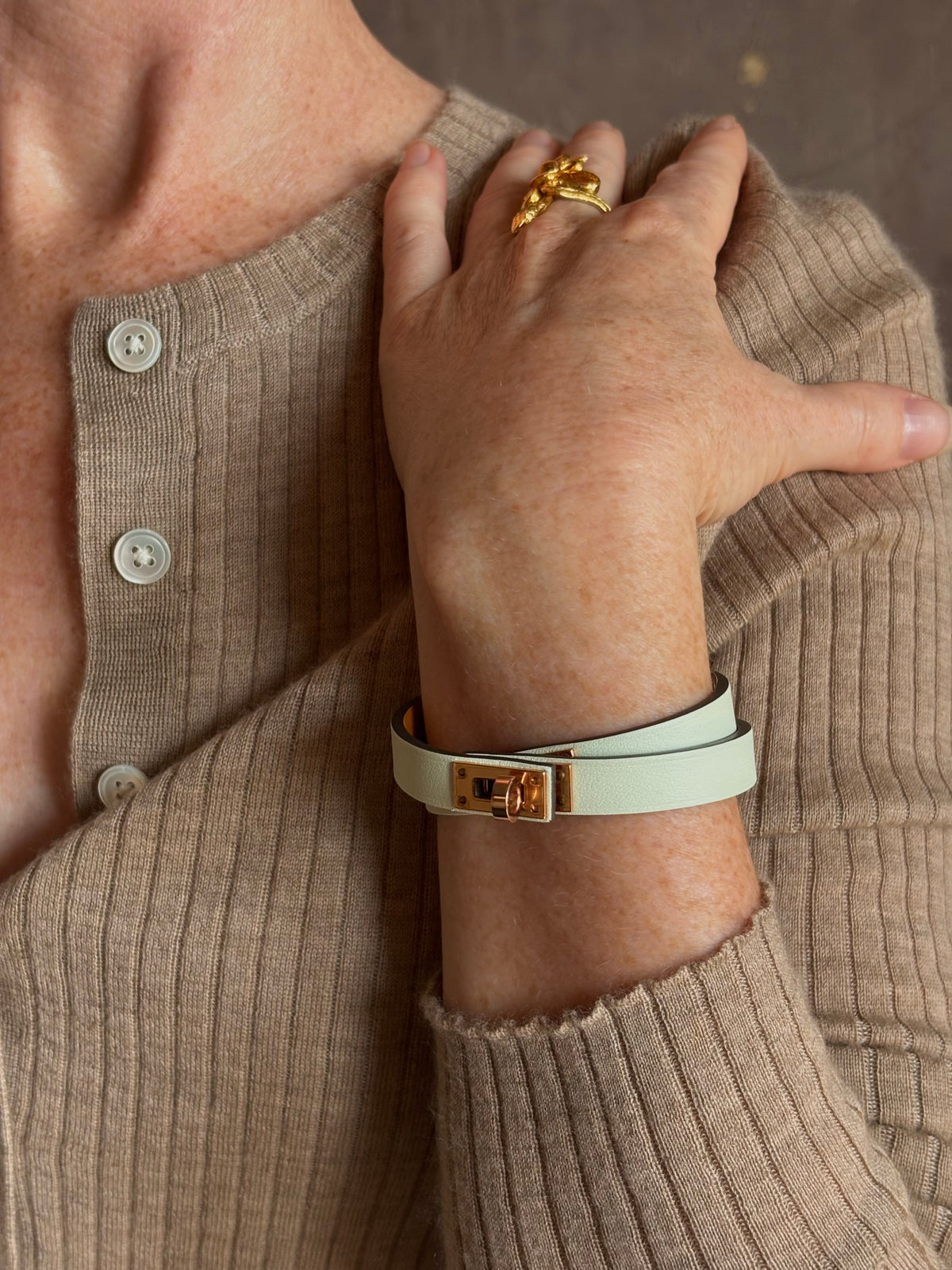 Mature woman wearing Hermès' Mini Kelly Double Tour Wrap Bracelet in Vert d'Eau & Rose Gold pristine, never-worn leather with the iconic Kelly turn-lock. Rare, collectible French luxury