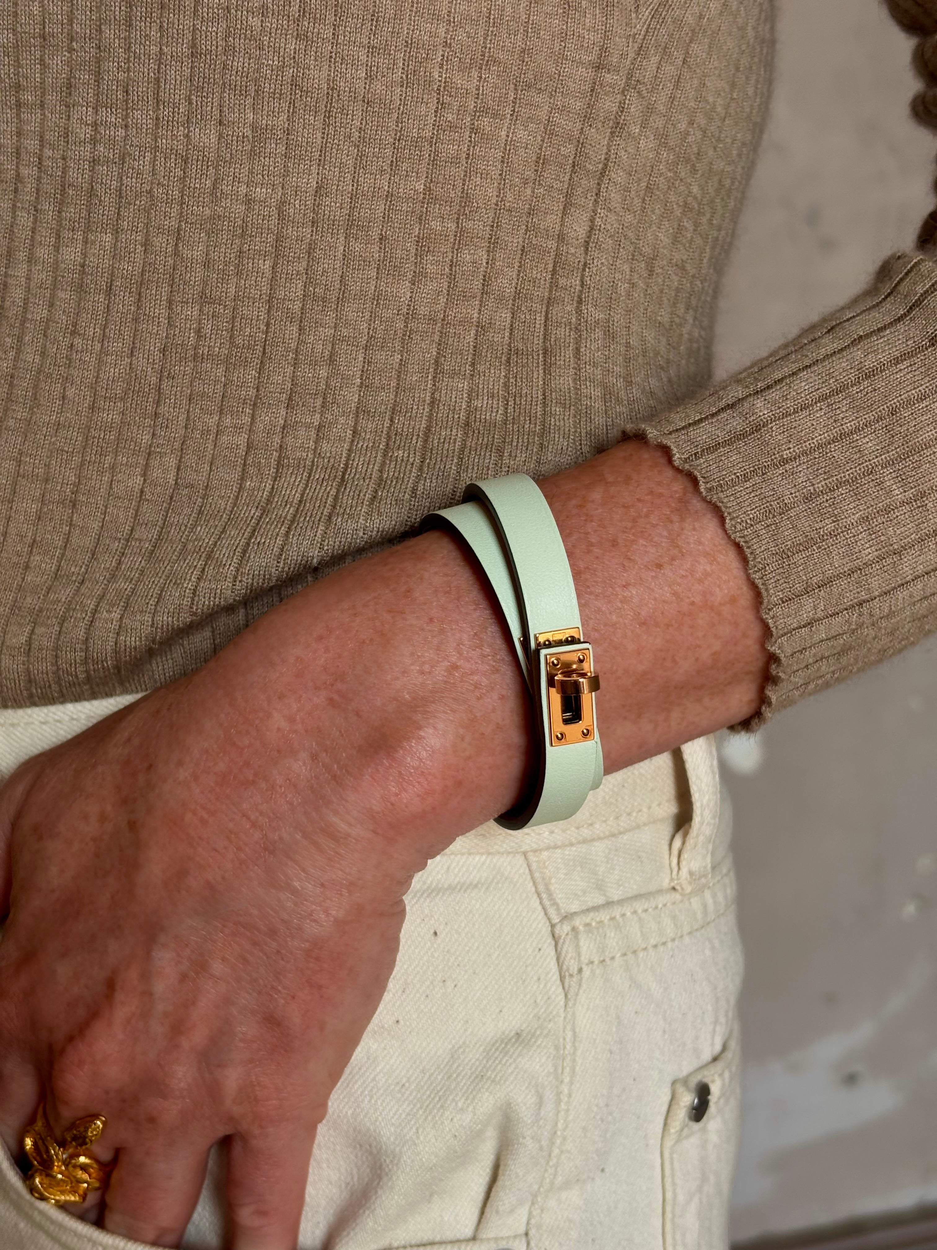 Mature woman wearing Hermès' Mini Kelly Double Tour Wrap Bracelet in Vert d'Eau & Rose Gold pristine, never-worn leather with the iconic Kelly turn-lock. Rare, collectible French luxury
