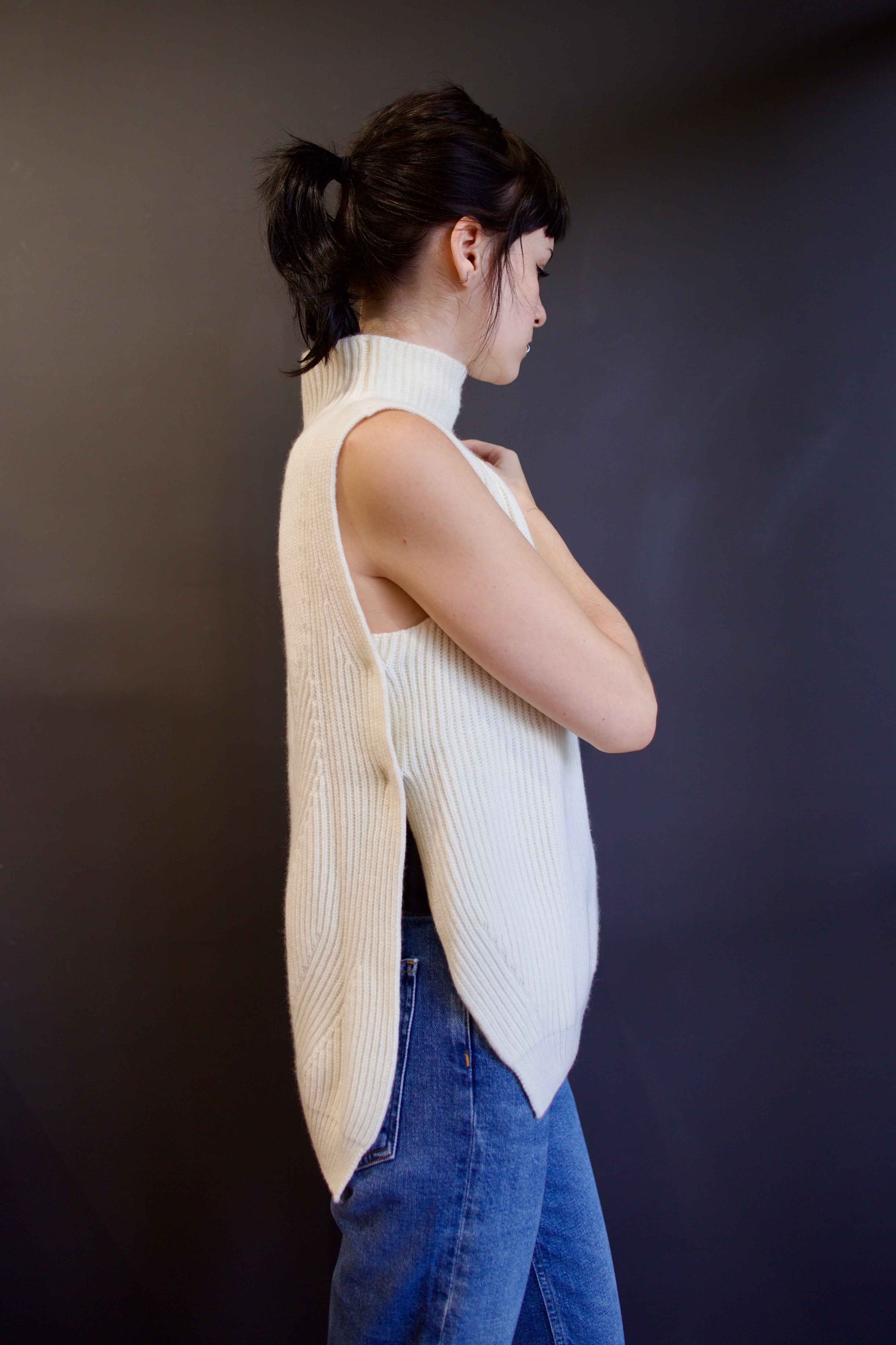 Model wearing a Kujten Erika cream-colored sleeveless cashmere sweater  with a mock neck and beautifully crafted