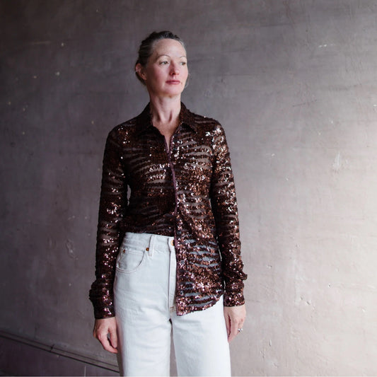 Image of a woman wearing the Le Superbe espresso sequin long sleeve button down sheer shirt with tiger's eye snaps and piping at the cuff.