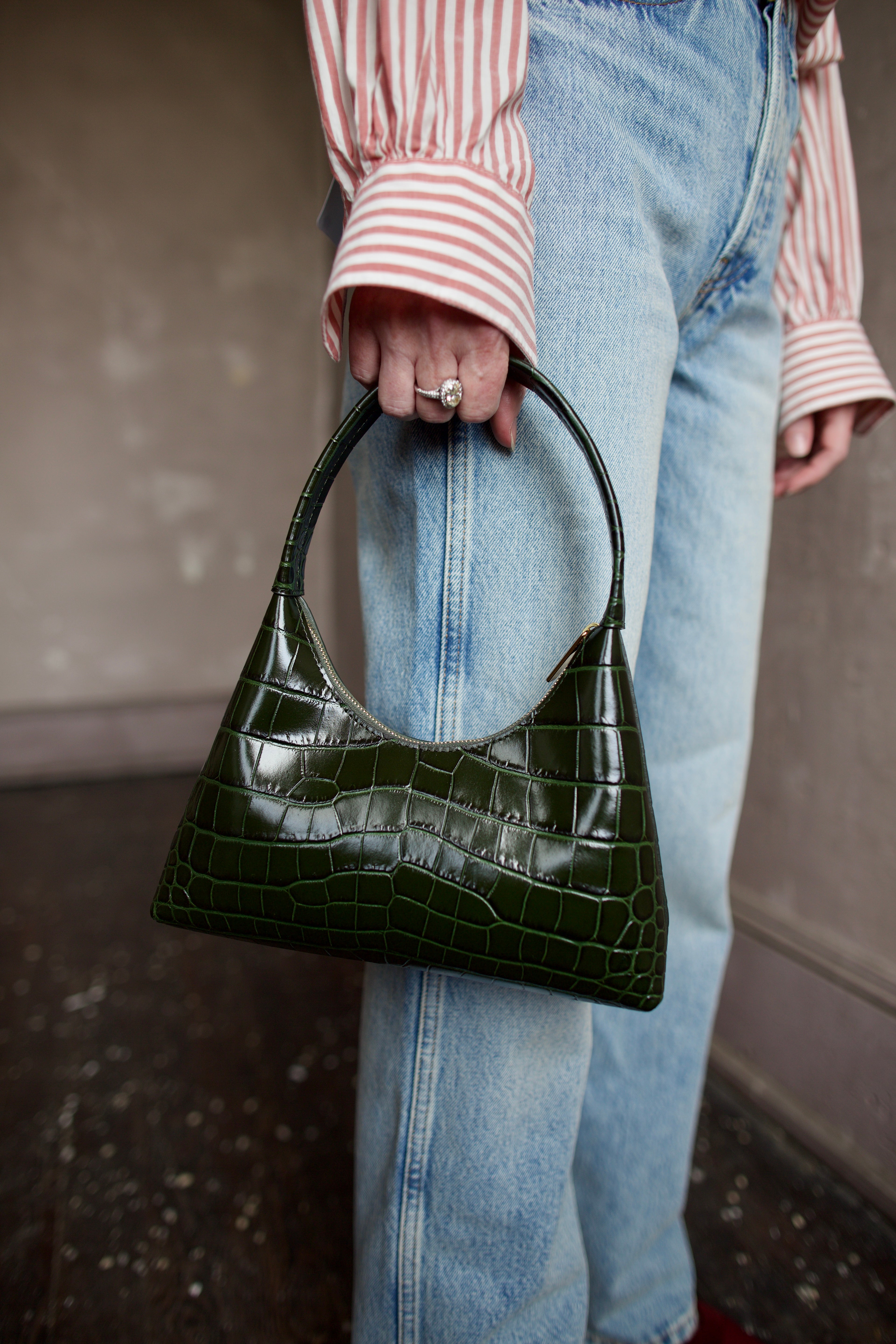 Image featuring a woman carrying the Mini Candy handbag by Mansur Gavriel in deep green with a gold finish zip closure and a croc texture.