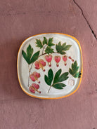 A square ceramic tile with botanical pressed bleeding heart flower stem and foliage on cream clay by NC artist