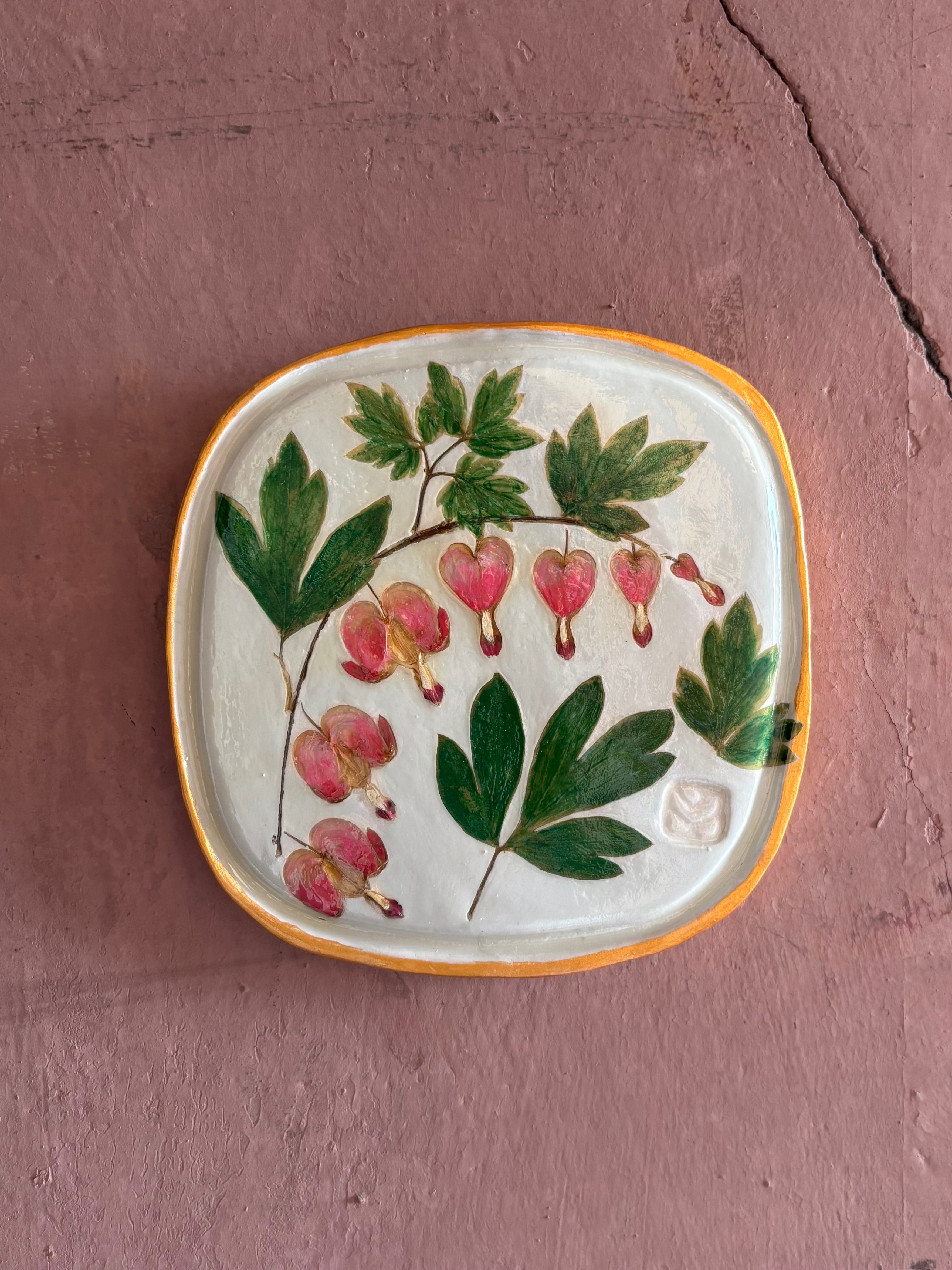 A square ceramic tile with botanical pressed bleeding heart flower stem and foliage on cream clay by NC artist