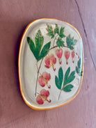 A square ceramic tile with botanical pressed bleeding heart flower stem and foliage on cream clay by NC artist