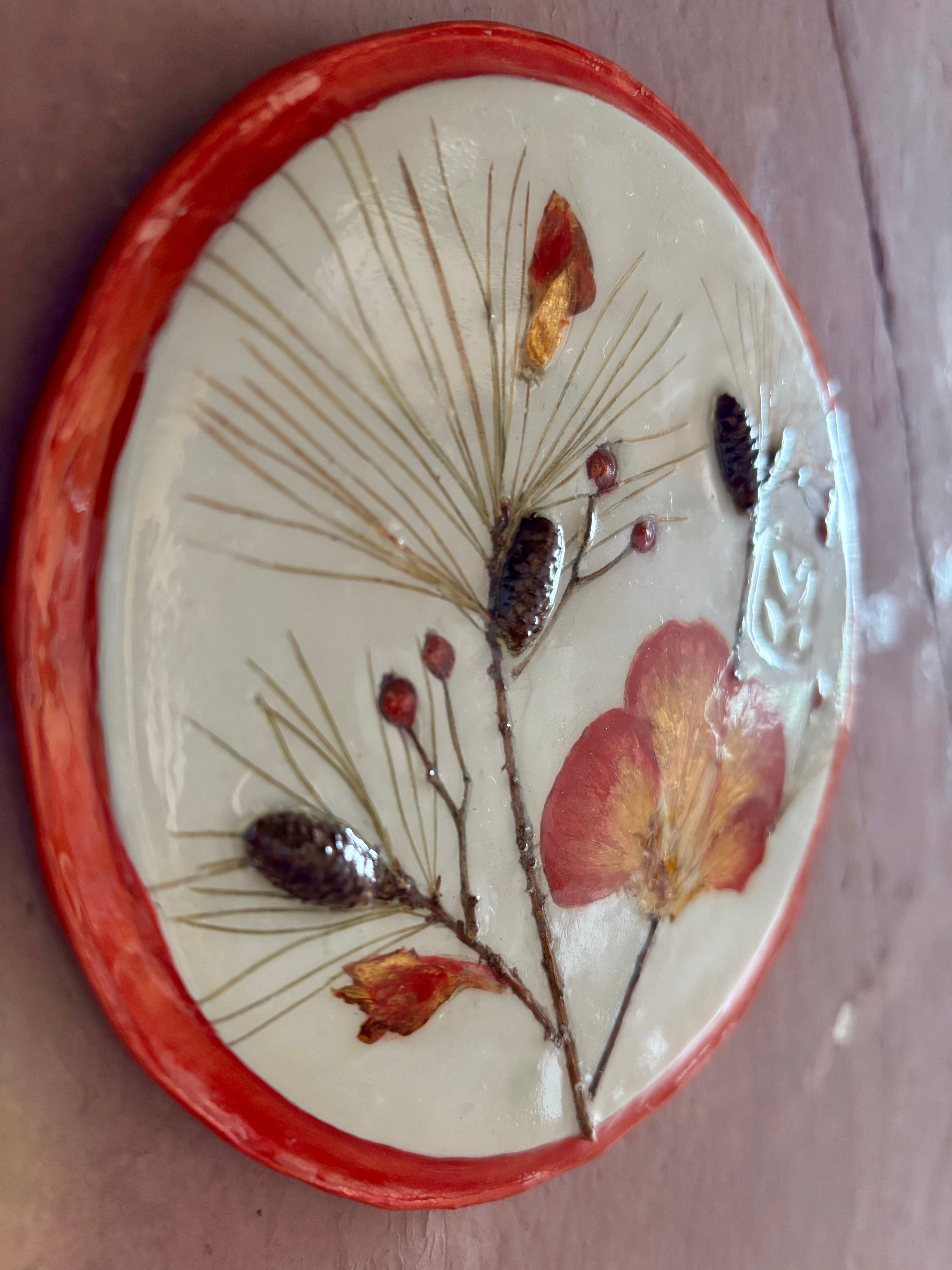 A round ceramic wall plaque pressed botanical elements holly azalea pine needles pinecones and red berries