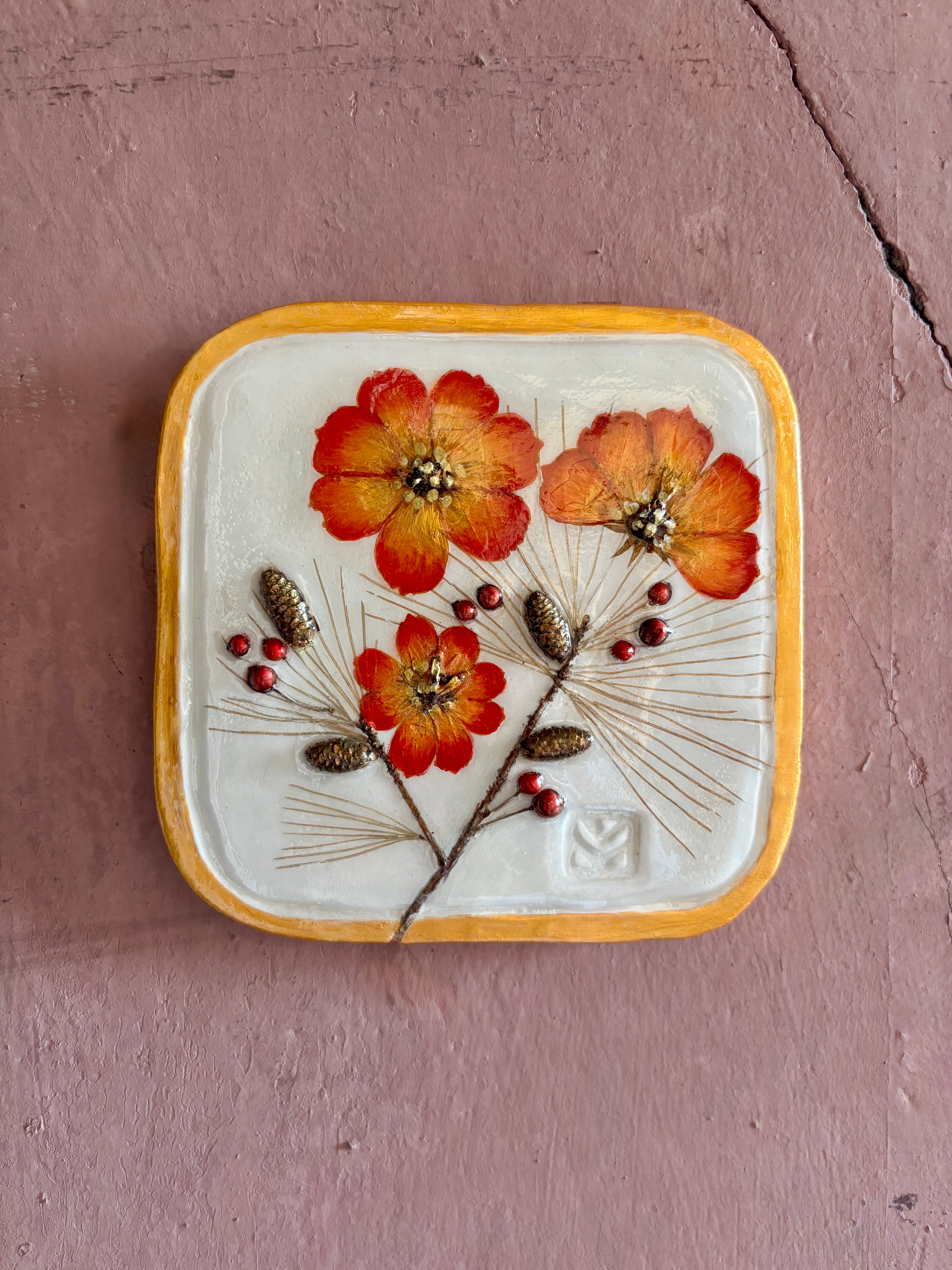 A square ceramic wall plaque pressed botanical elements holly cosmos pine needles pinecones and red berries