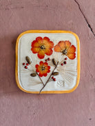 A square ceramic wall plaque pressed botanical elements holly cosmos pine needles pinecones and red berries