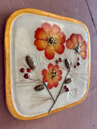 A square ceramic wall tile pressed botanical elements holly cosmos pine needles pinecones and red berries