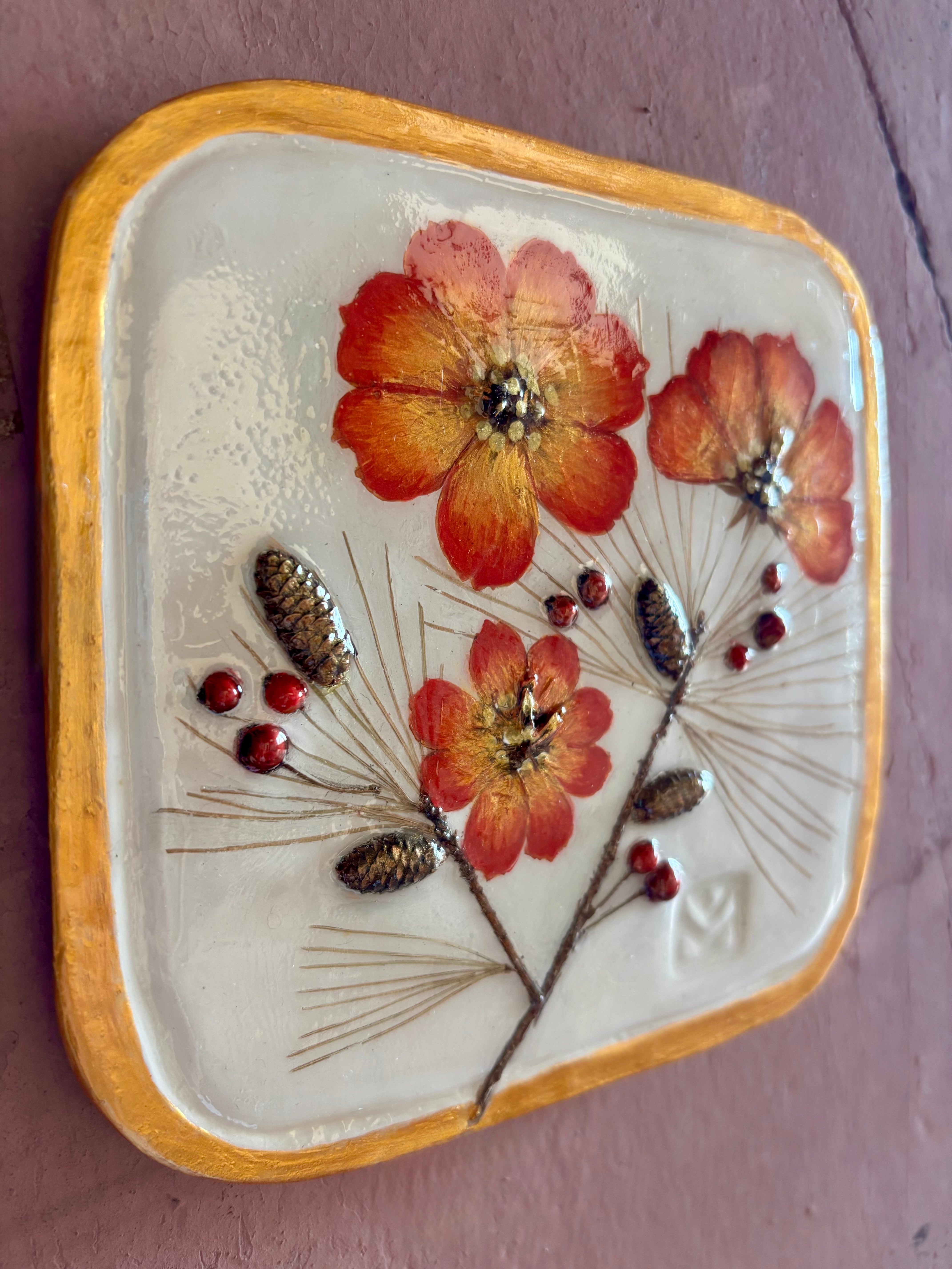 A square ceramic wall tile pressed botanical elements holly cosmos pine needles pinecones and red berries