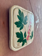 A square ceramic tile with botanical pressed bleeding heart flower stem and foliage on cream clay by NC artist