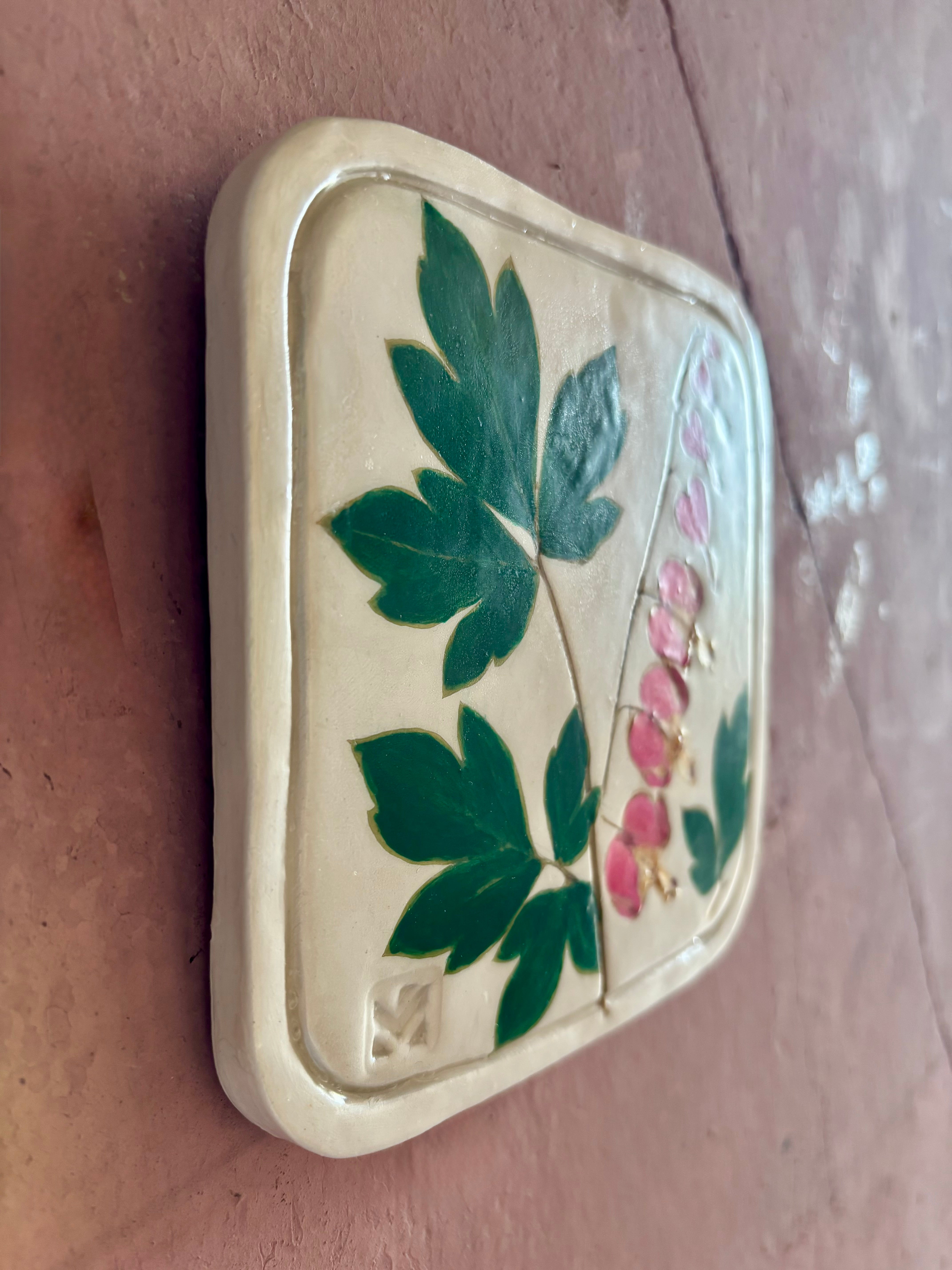 A square ceramic tile with botanical pressed bleeding heart flower stem and foliage on cream clay by NC artist