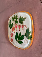 A square ceramic tile with botanical pressed bleeding heart flower stem and foliage on cream clay by NC artist