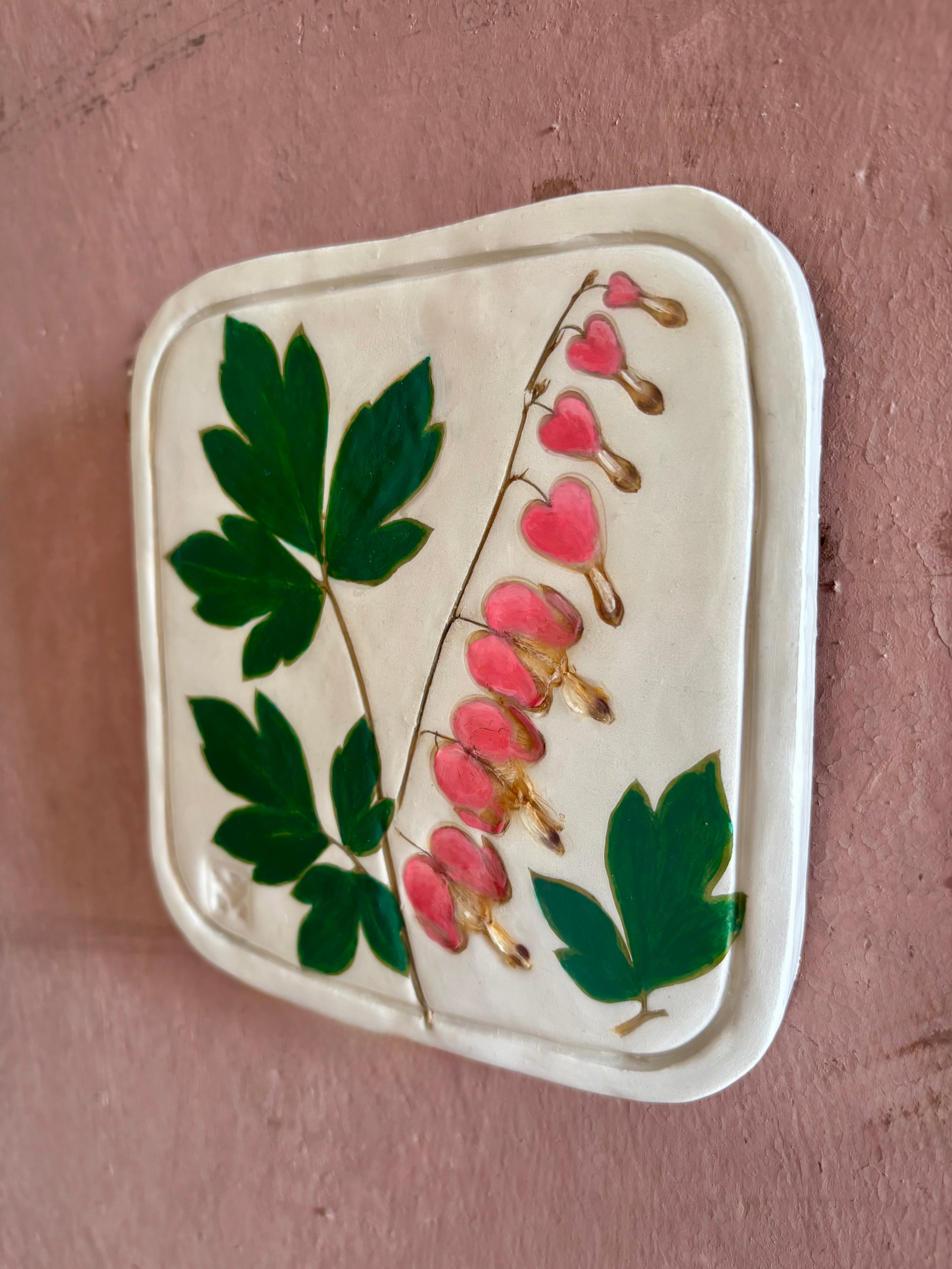A square ceramic tile with botanical pressed bleeding heart flower stem and foliage on cream clay by NC artist