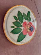 A round white ceramic tile with sappora rhododendron bloom botanical press green leaves and hand painted gold rim