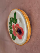 A round white ceramic tile with sappora rhododendron bloom botanical press green leaves and hand painted gold rim