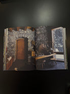 An open book or magazine spread showing a rustic interior scene with stone walls wooden door table window