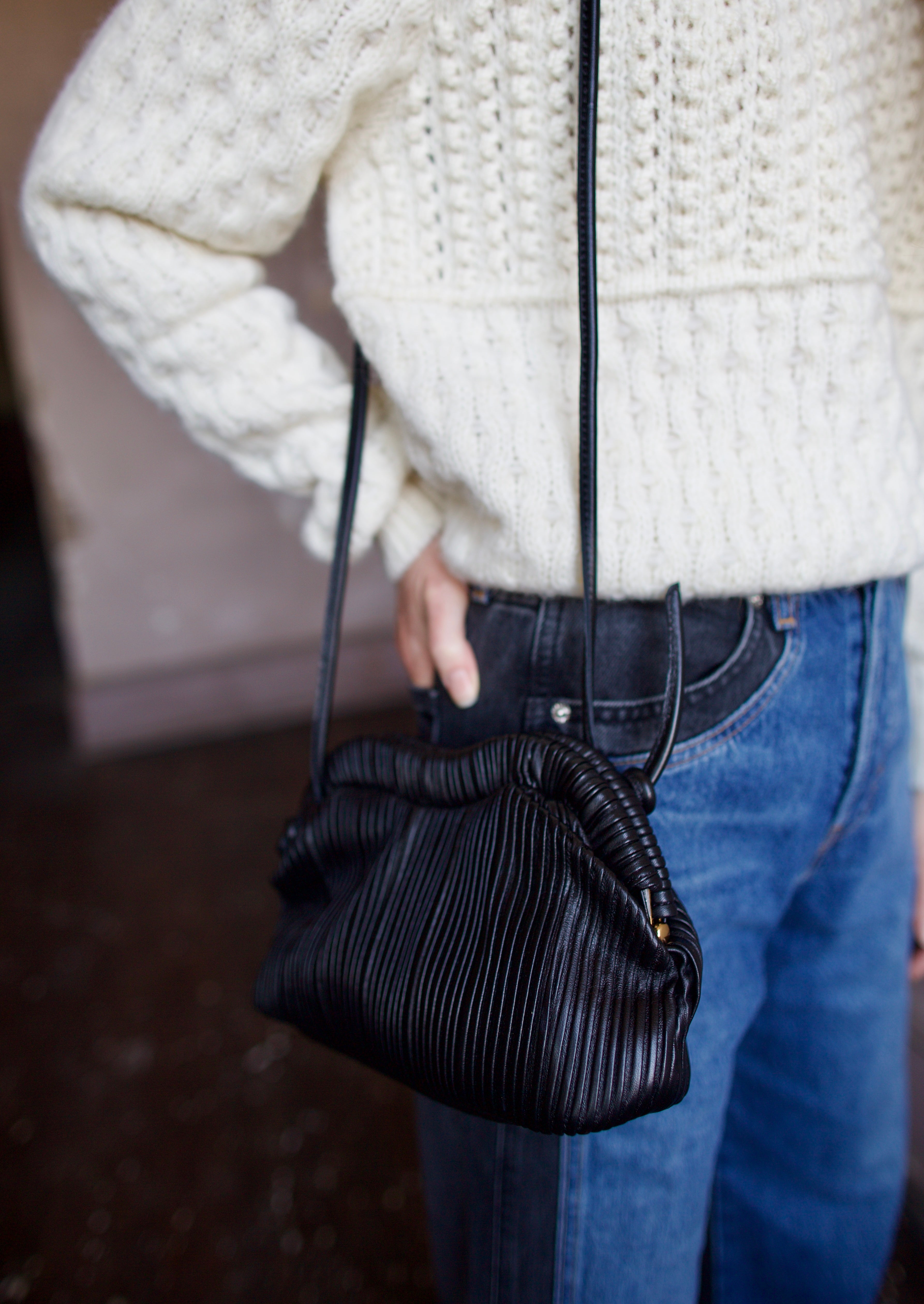 Image featuring a woman wearing the Baci handbag by Mansur Gavriel in black with a magnetic closure, adjustable crossbody strap and intricate pintucked leather across entire hand bag.