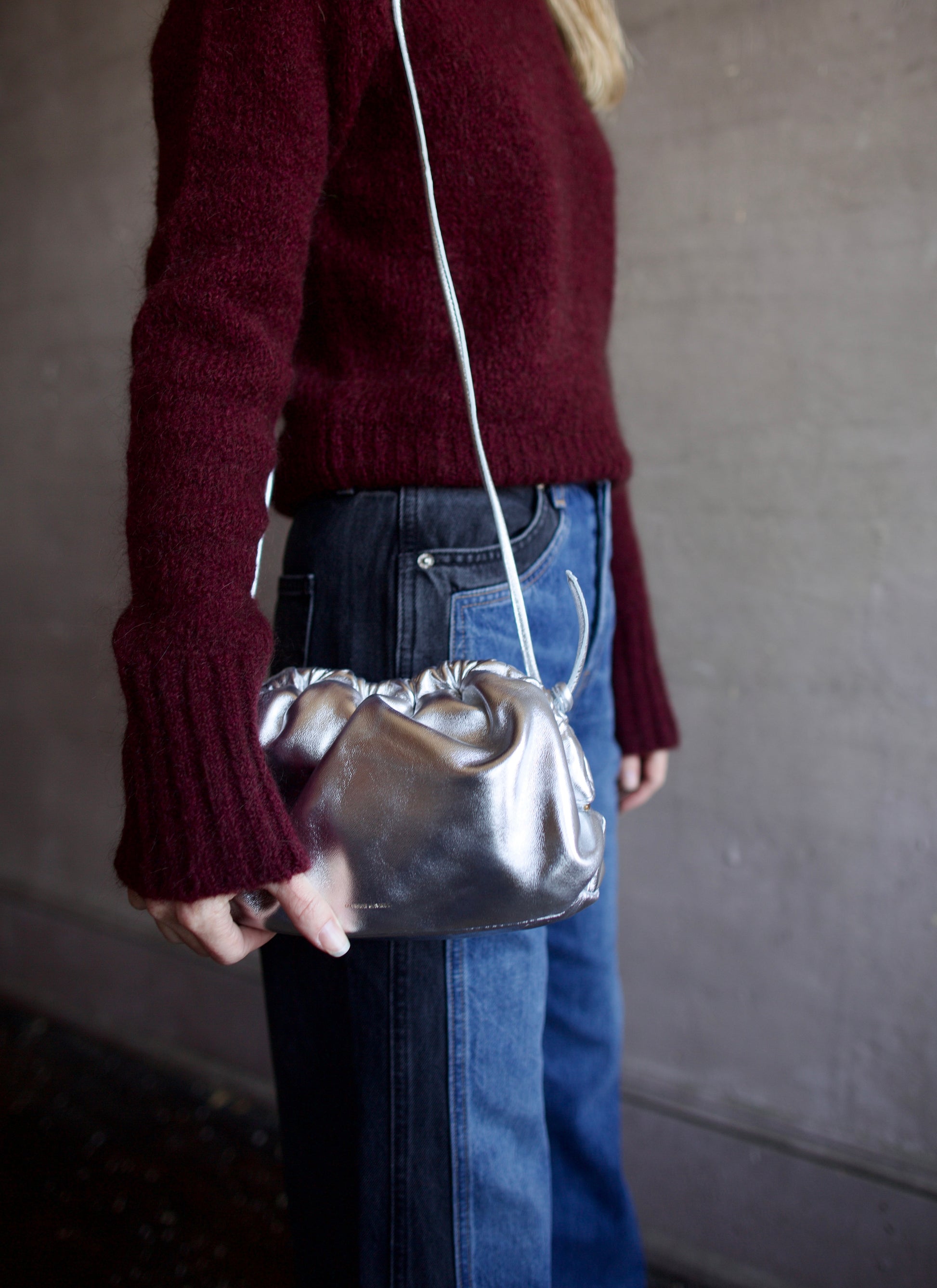 Image featuring a woman wearing the Mini Cloud handbag by Mansur Gavriel in silver with a magnetic closure and adjustable crossbody strap.