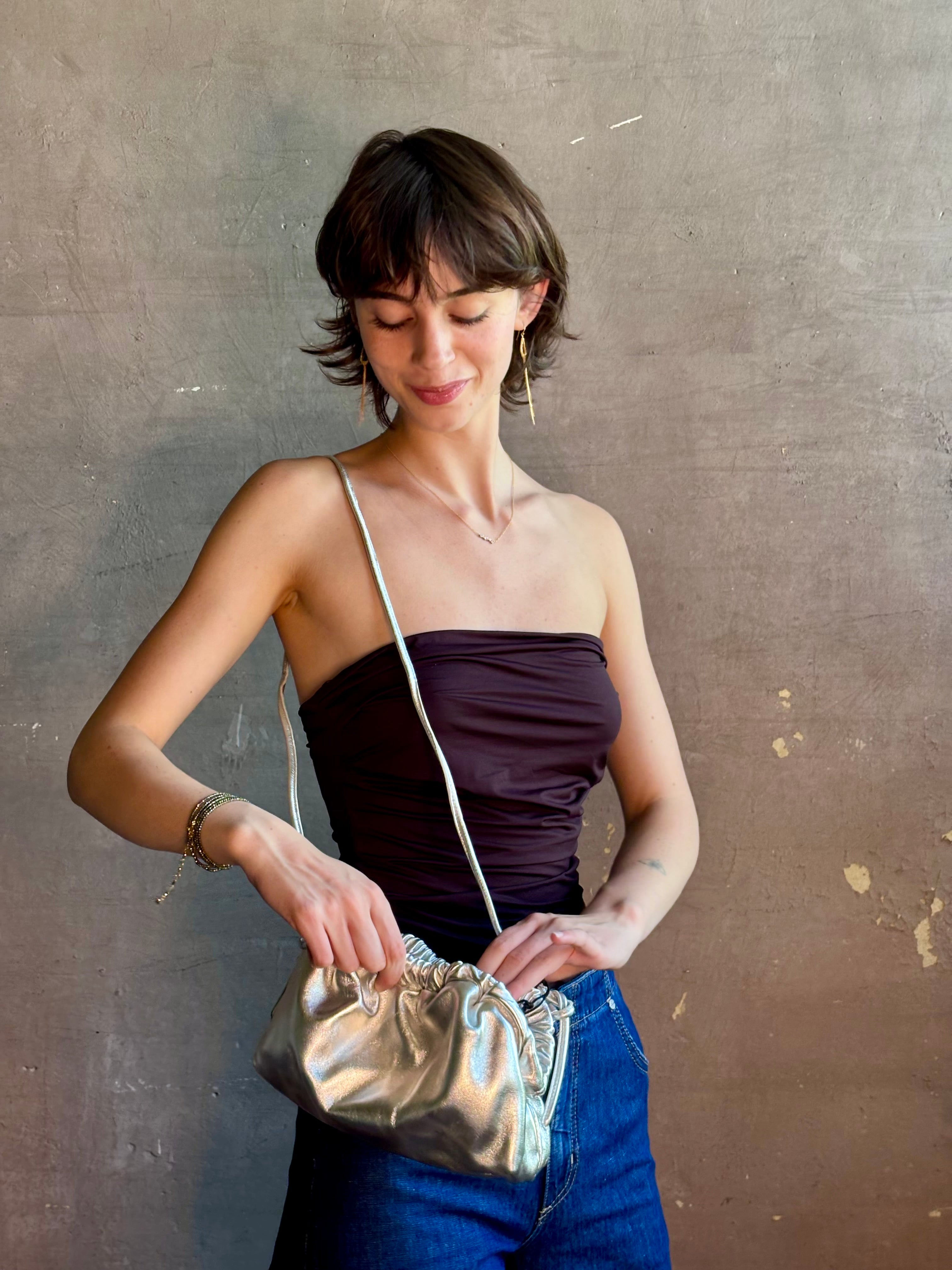 Woman wearing the Italian leather Mini Cloud crossbody by high-end designer Mansur Gavriel in metallic silver with removeable shoulder strap that can also double as a clutch