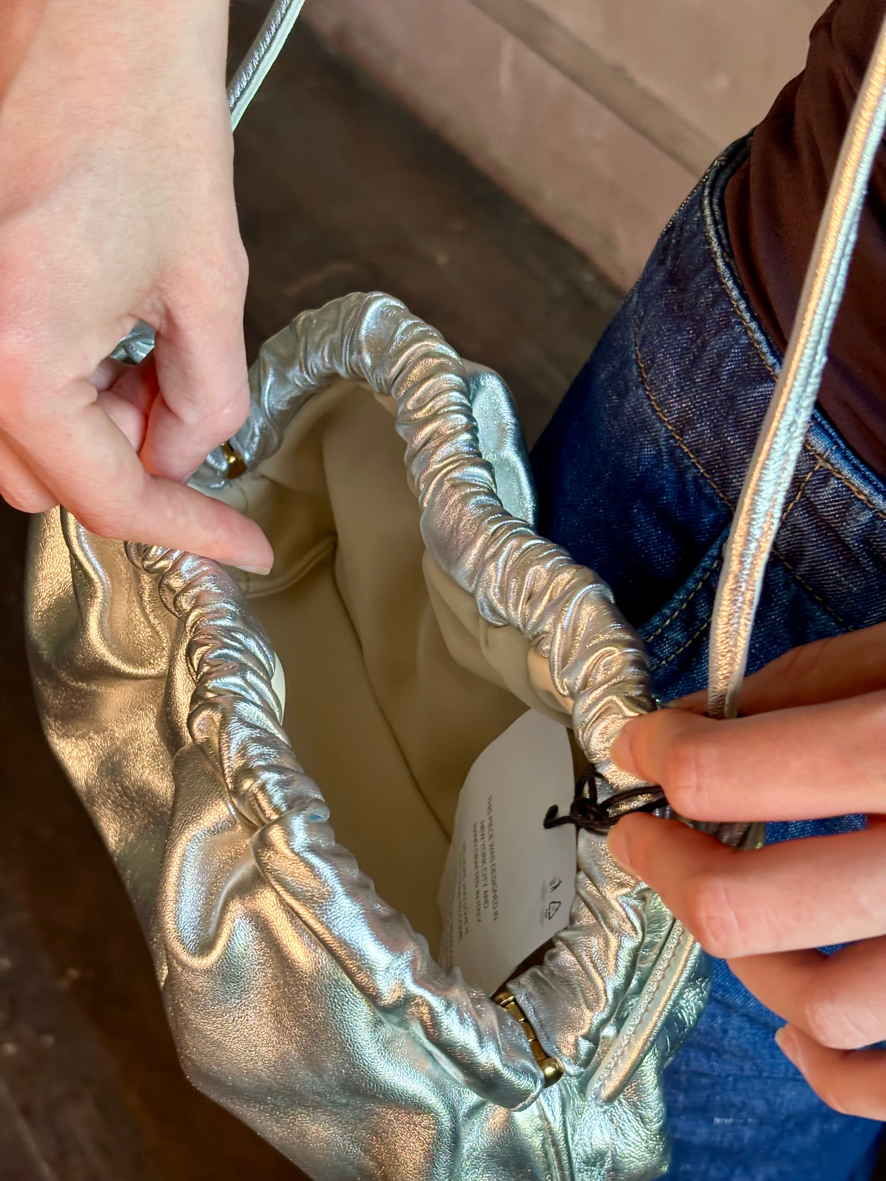 Woman wearing the Italian leather Mini Cloud crossbody by high-end designer Mansur Gavriel in metallic silver with removeable shoulder strap that can also double as a clutch