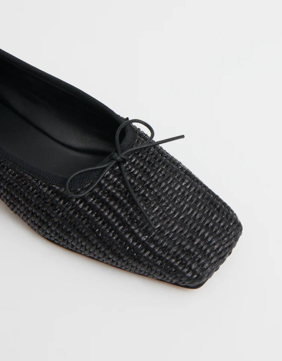 Close up image of black woven raffia ballet flats with a square toe and bowtie by high-end footwear designer Mansur 