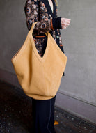 Image featuring a woman holding the Mansur Gavriel soft hobo with a double tie closure, oversized and a shoulder handle with v-detail in light brown suede leather.