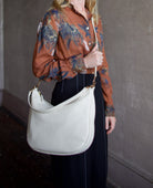 Image featuring a woman wearing the Swing Bag by Mansur Gavriel in cream and  trimmed with gold finish hardware zip closure, adjustable crossbody strap and shoulder strap.