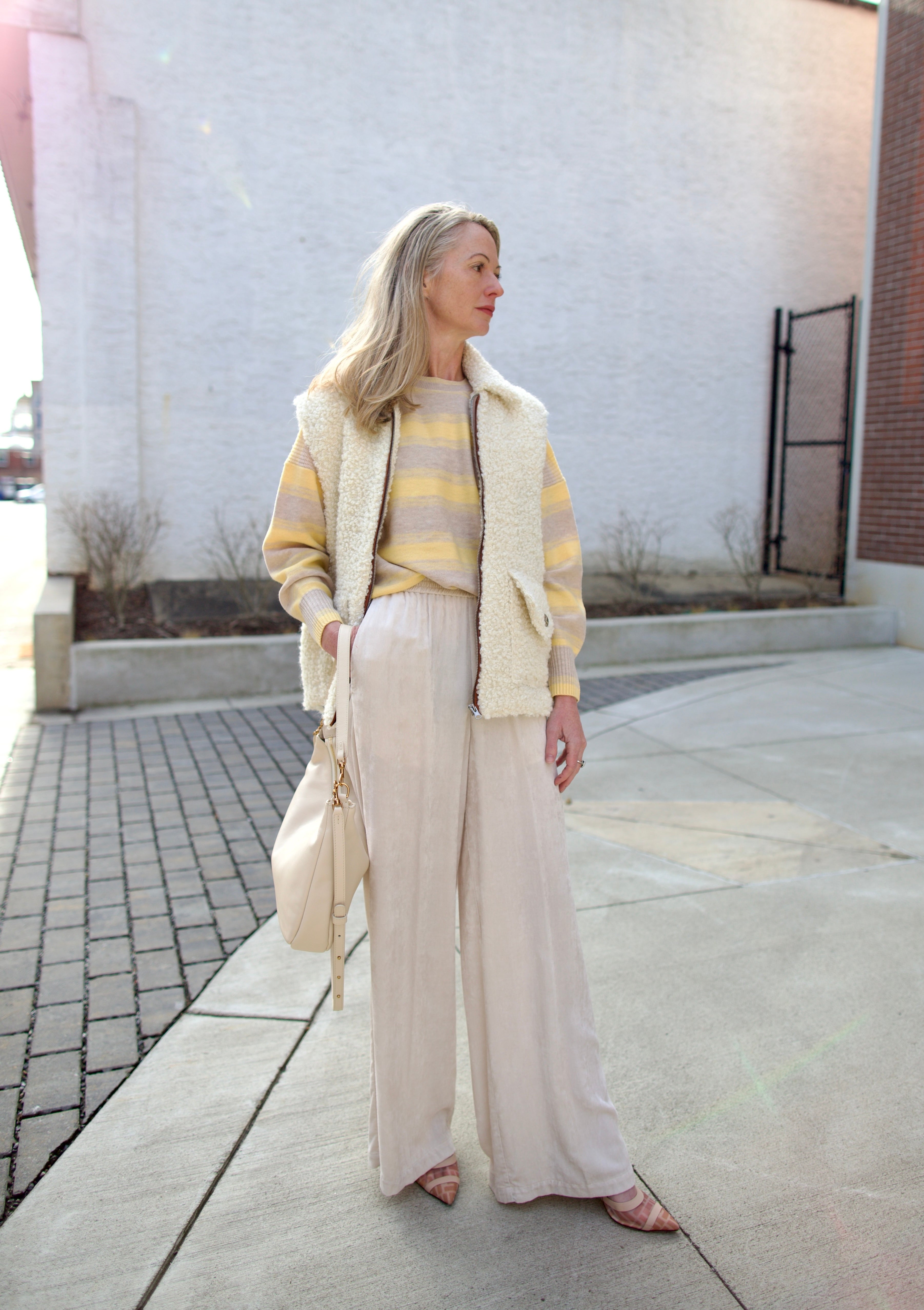Mature woman holding Mansur Gavriel Swing leather bag in Ivory a warm winter white with two optional leather straps for a versitale handbag ready for any adventure