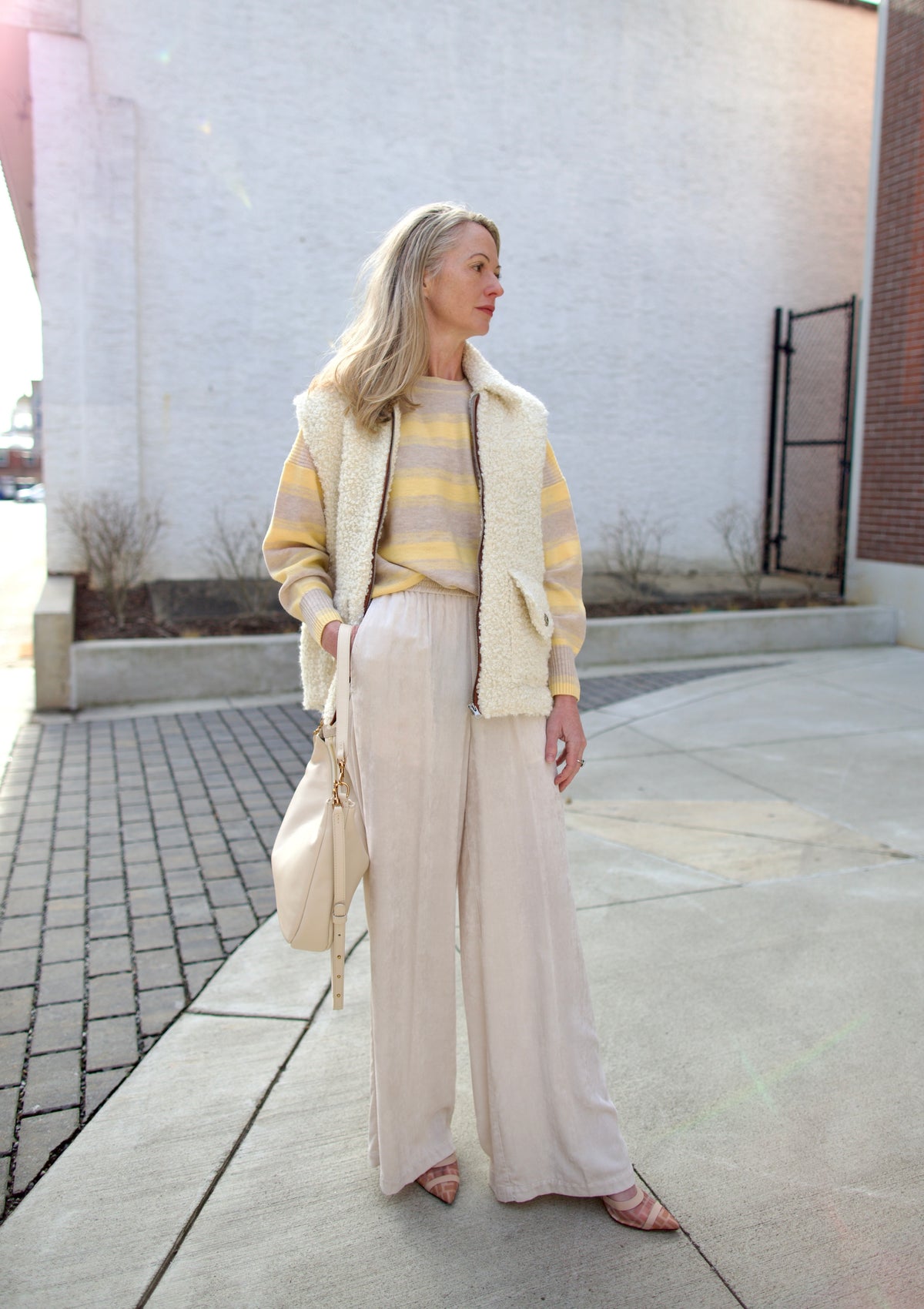 Mature woman holding Mansur Gavriel Swing leather bag in Ivory a warm winter white with two optional leather straps for a versitale handbag ready for any adventure