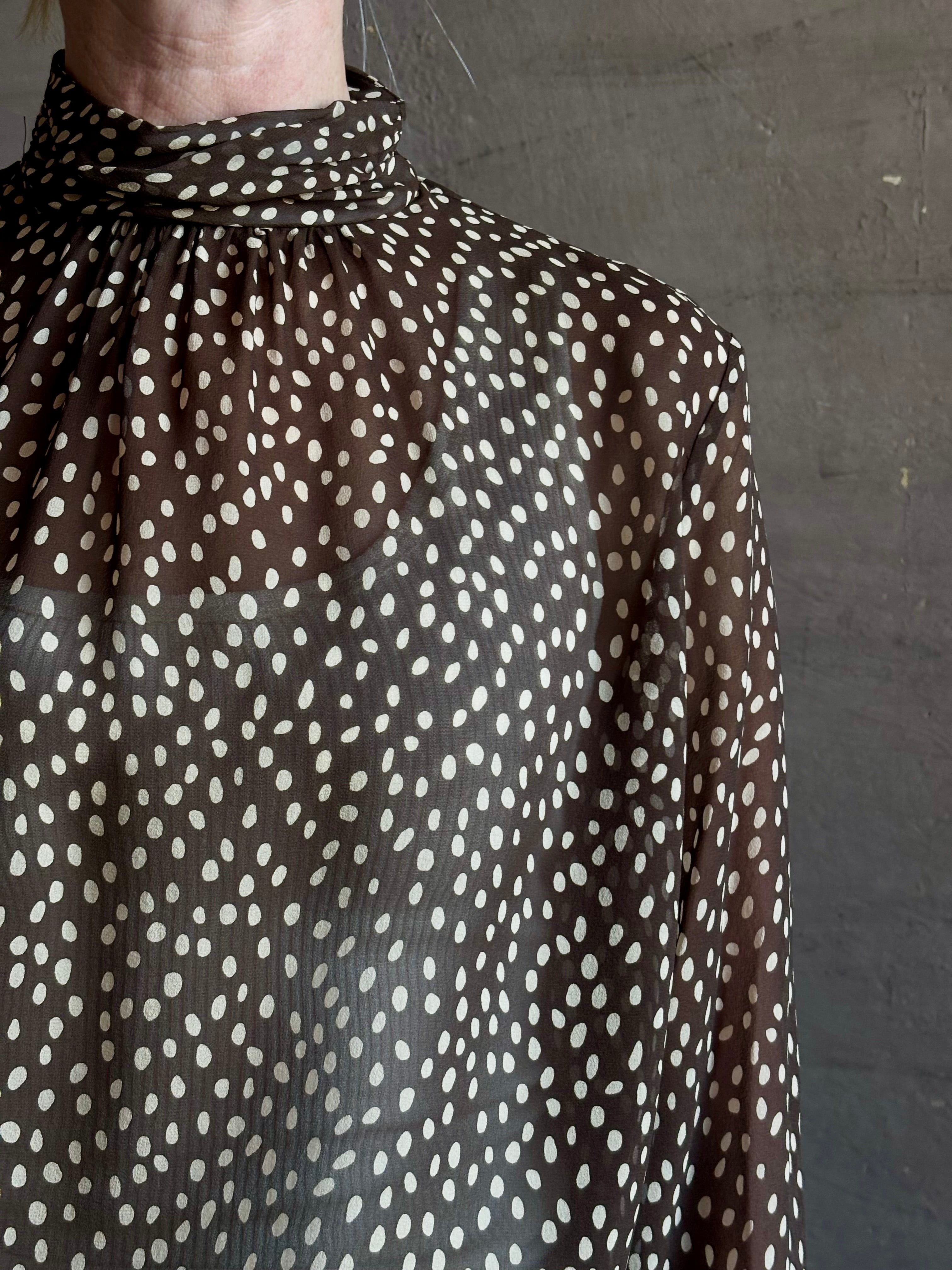 Mature woman wearing Nili Lotan Silk Demie Blouse in Brown/Cream Wild Dots sheer mock neck and keyhole back closure. Made in the USA