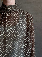 Mature woman wearing Nili Lotan Silk Demie Blouse in Brown/Cream Wild Dots sheer mock neck and keyhole back closure. Made in the USA