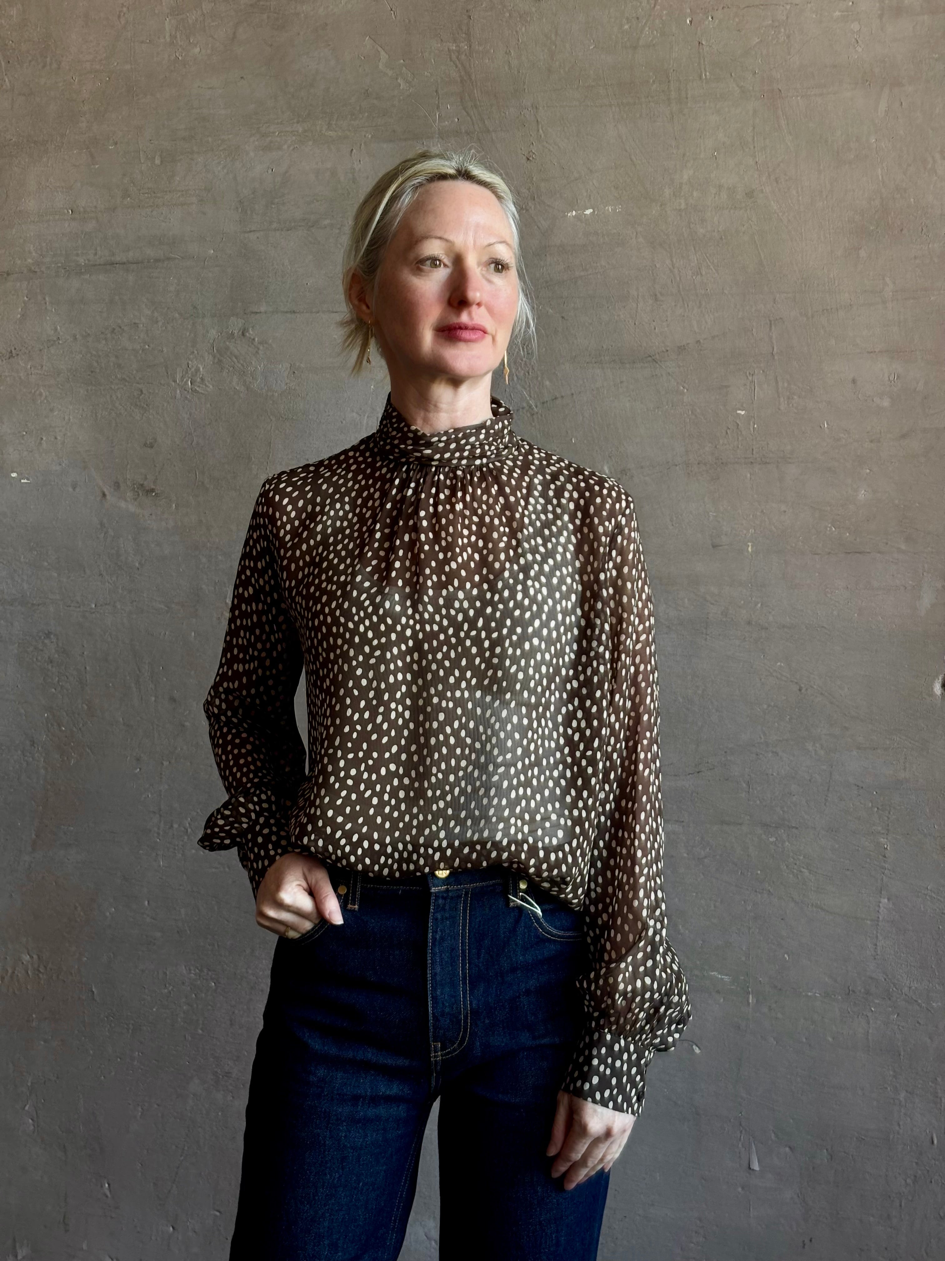 Mature woman wearing Nili Lotan Silk Demie Blouse in Brown/Cream Wild Dots sheer mock neck and keyhole back closure. Made in the USA