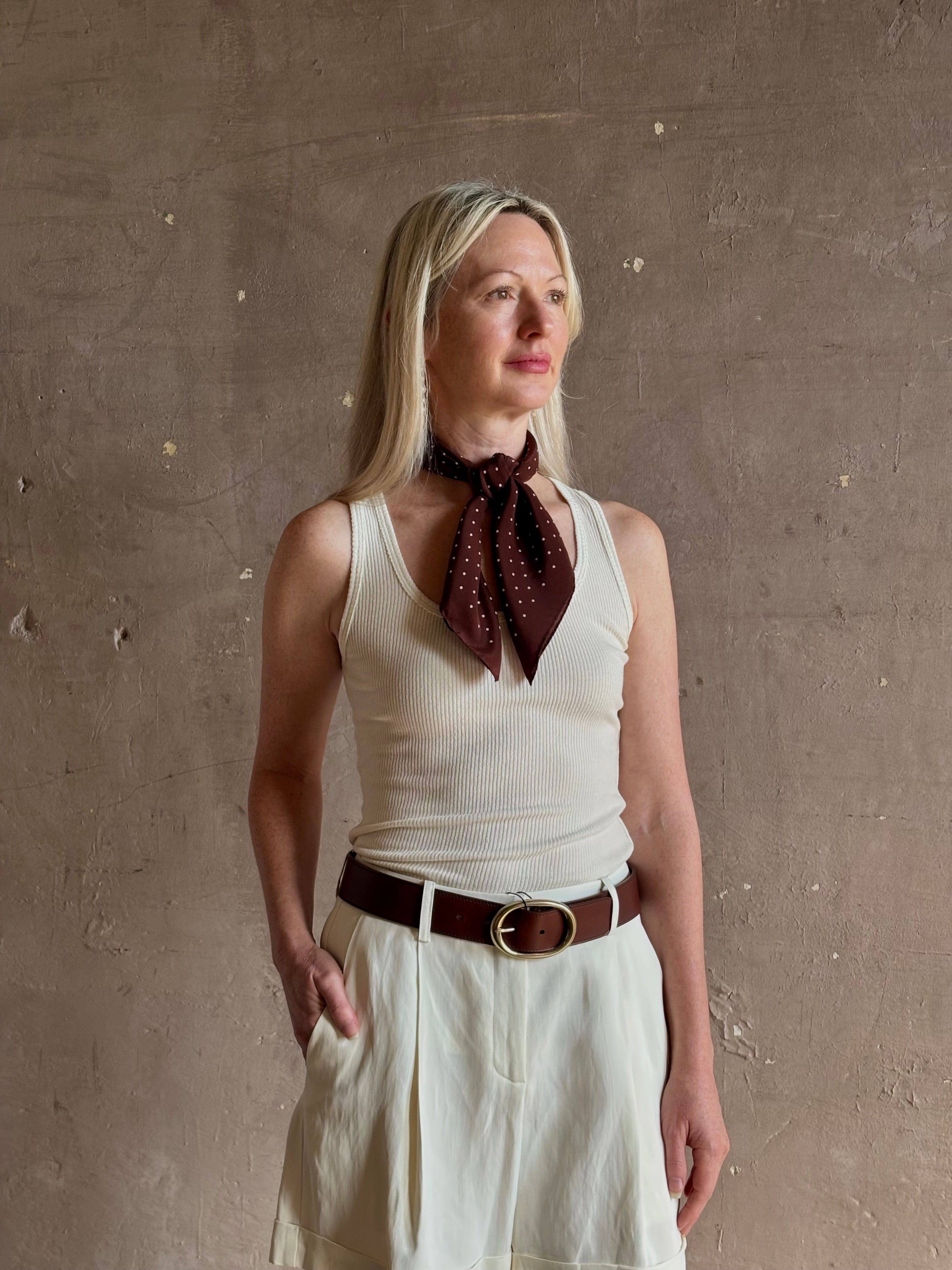 A mature woman wearing and brown scarf with small white polka-dot pattern as a neck tie