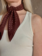 A mature woman wearing and brown scarf with small white polka-dot pattern as a neck tie