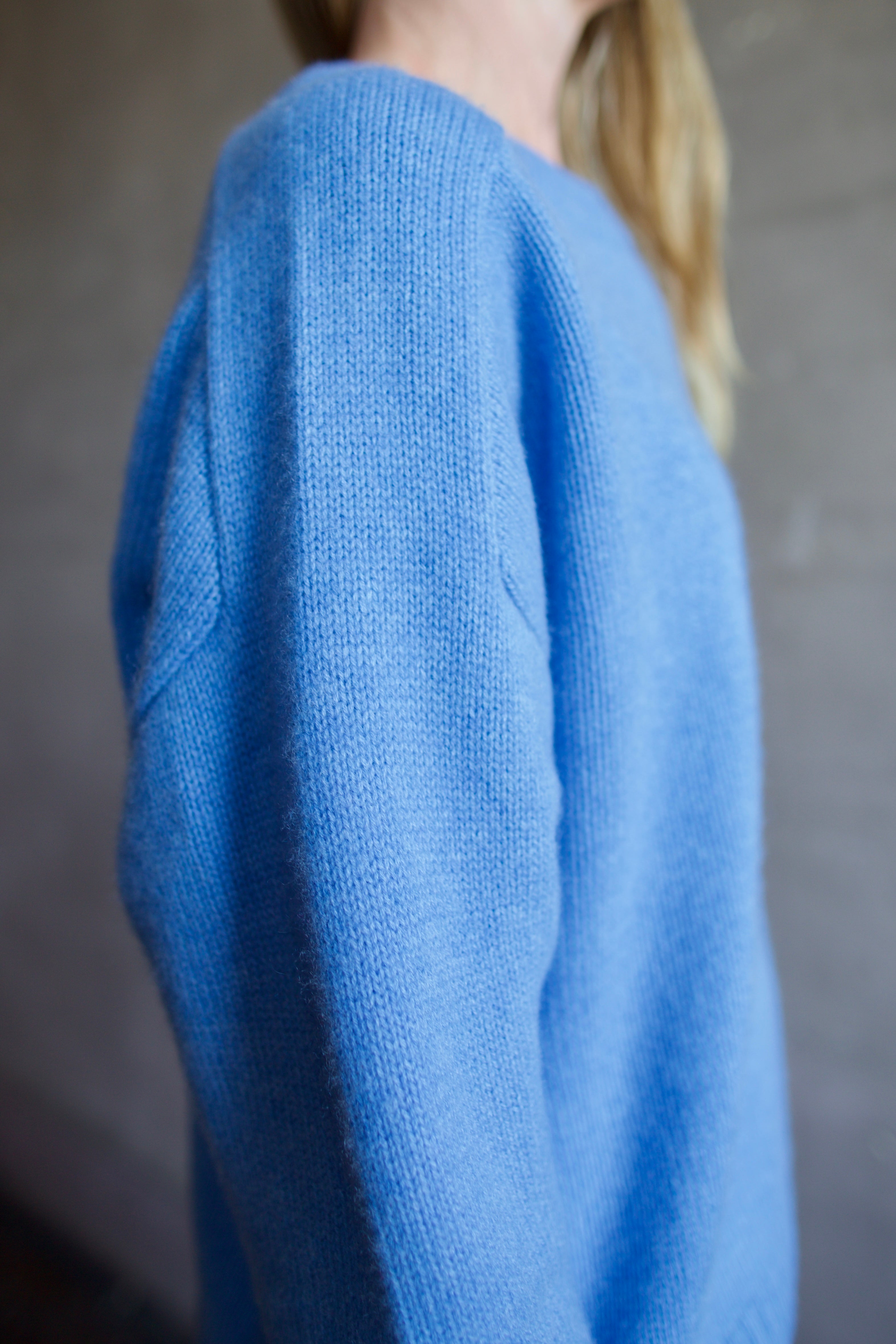 Image featuring a woman wearing the Super Luxe Cashmere Sweater by Naadam with a crew neck neckline, drop shoulder and a relaxed fit in bright blue.