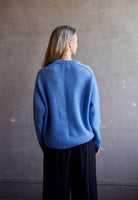 Image featuring a woman wearing the Super Luxe Cashmere Sweater by Naadam with a crew neck neckline, drop shoulder and a relaxed fit in bright blue.