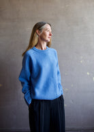 Image featuring a woman wearing the Super Luxe Cashmere Sweater by Naadam with a crew neck neckline, drop shoulder and a relaxed fit in bright blue.