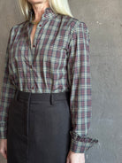 Mature woman wearing a long-sleeve plaid button-up shirt in muted burgundy, beige, and navy paired with a chocolate brown skirt perfect for Fall attire