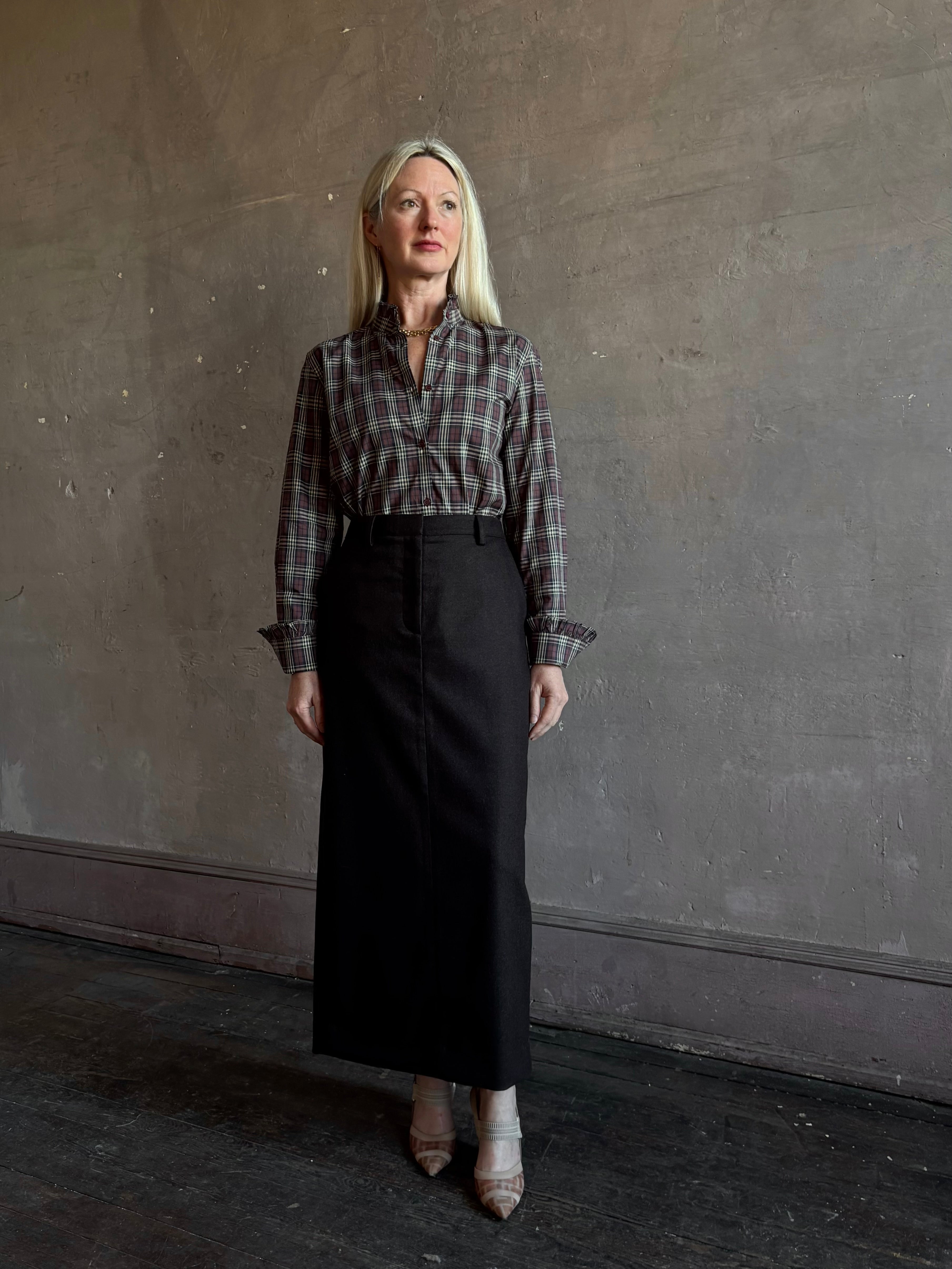 Mature woman wearing Nili Lotan’s Elio Shirt in burgundy and navy plaid print with ruffle-trimmed cuffs and collar tucked into a dark brown wool maxi pencil skirt for Fall