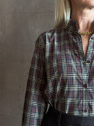 close-up image of a woman wearing a long-sleeve plaid button-up shirt in dark red, beige, and navy by Nili Lotan in Elio Ruffle collar feminine sihlouette