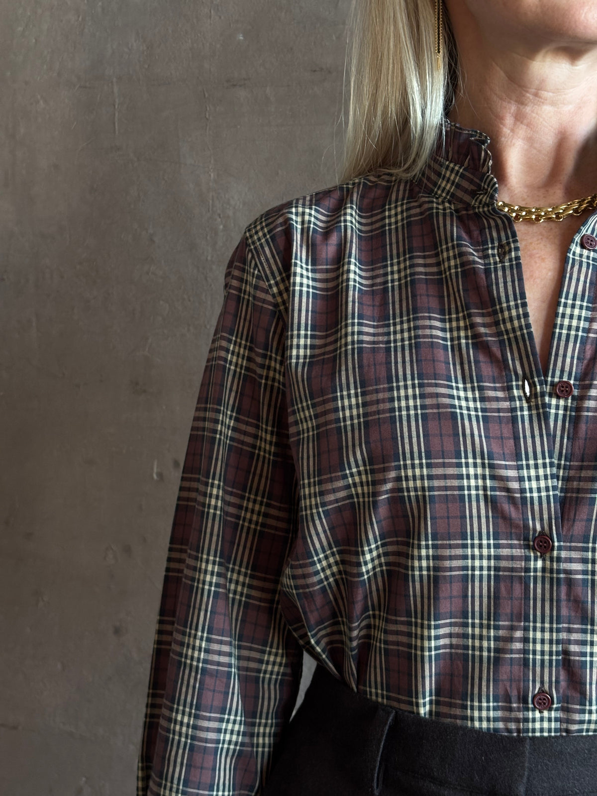 close-up image of a woman wearing a long-sleeve plaid button-up shirt in dark red, beige, and navy by Nili Lotan in Elio Ruffle collar feminine sihlouette