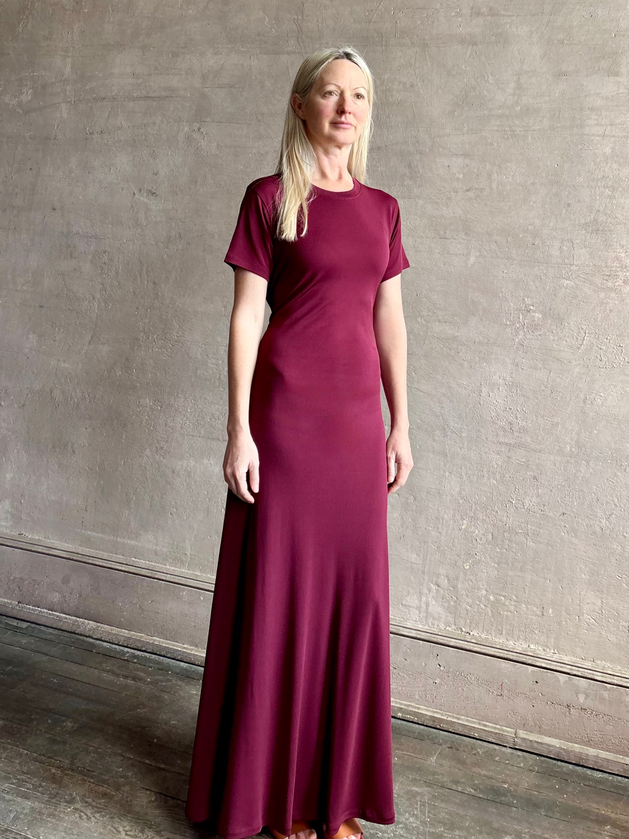 Mature woman wearing the Noelle designer dress from Proenza Schouler in a deep wine hue with elevated back draping detail short sleeves and crew neck