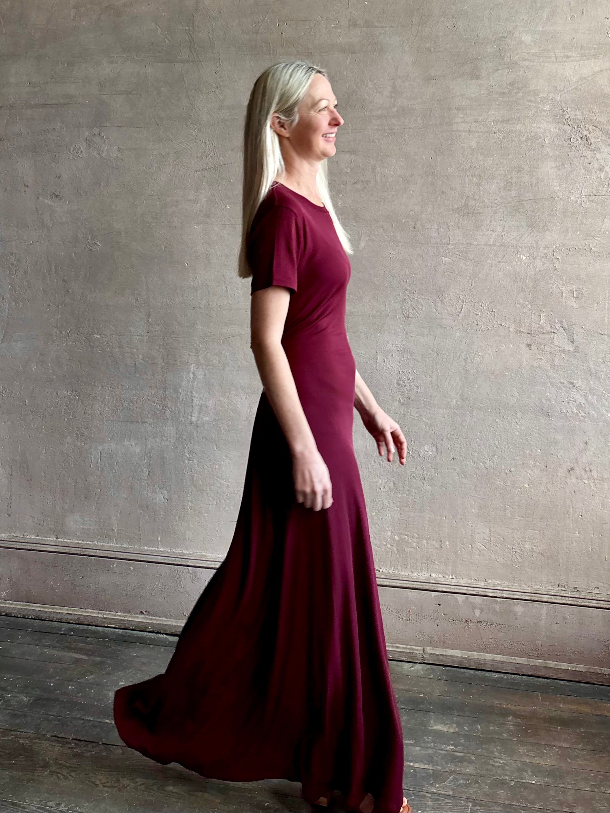 Mature woman wearing the Noelle designer dress from Proenza Schouler in a deep wine hue with elevated back draping detail short sleeves and crew neck