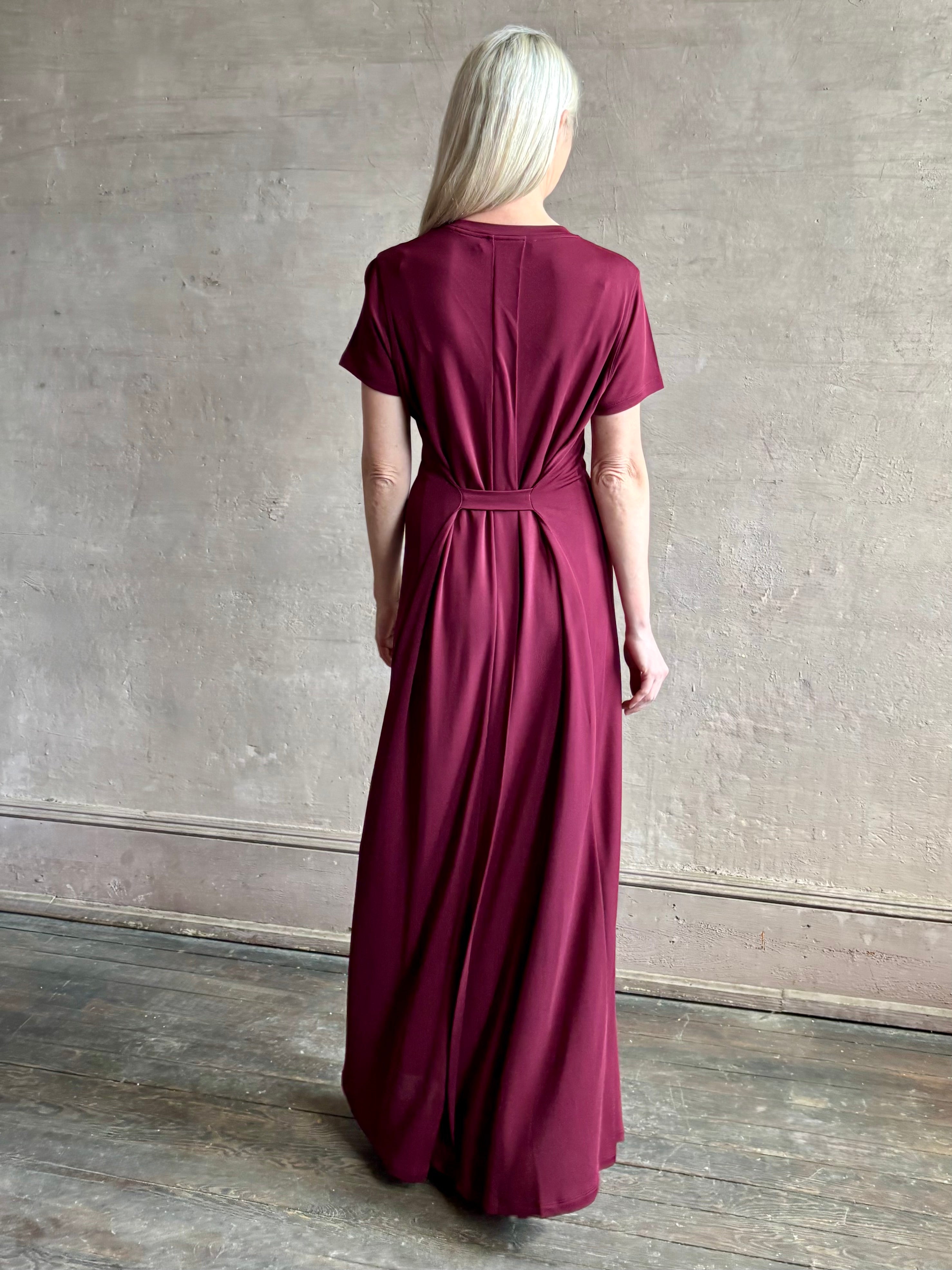 Mature woman wearing the Noelle designer dress from Proenza Schouler in a deep wine hue with elevated back draping detail short sleeves and crew neck
