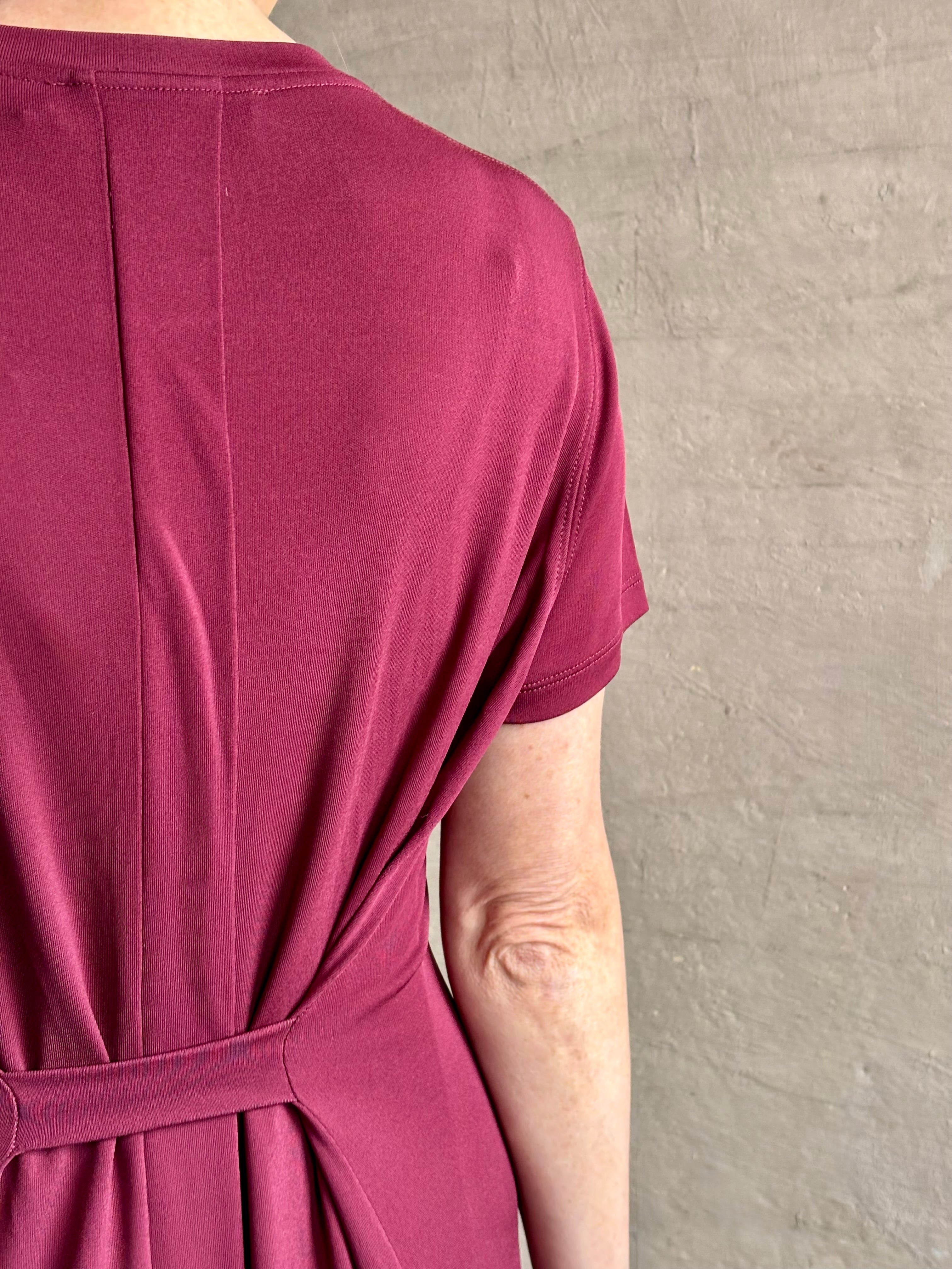 Mature woman wearing the Noelle designer dress from Proenza Schouler in a deep wine hue with elevated back draping detail short sleeves and crew neck