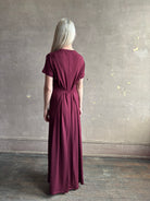 Mature woman wearing the Noelle designer dress from Proenza Schouler in a deep wine hue with elevated back draping detail short sleeves and crew neck