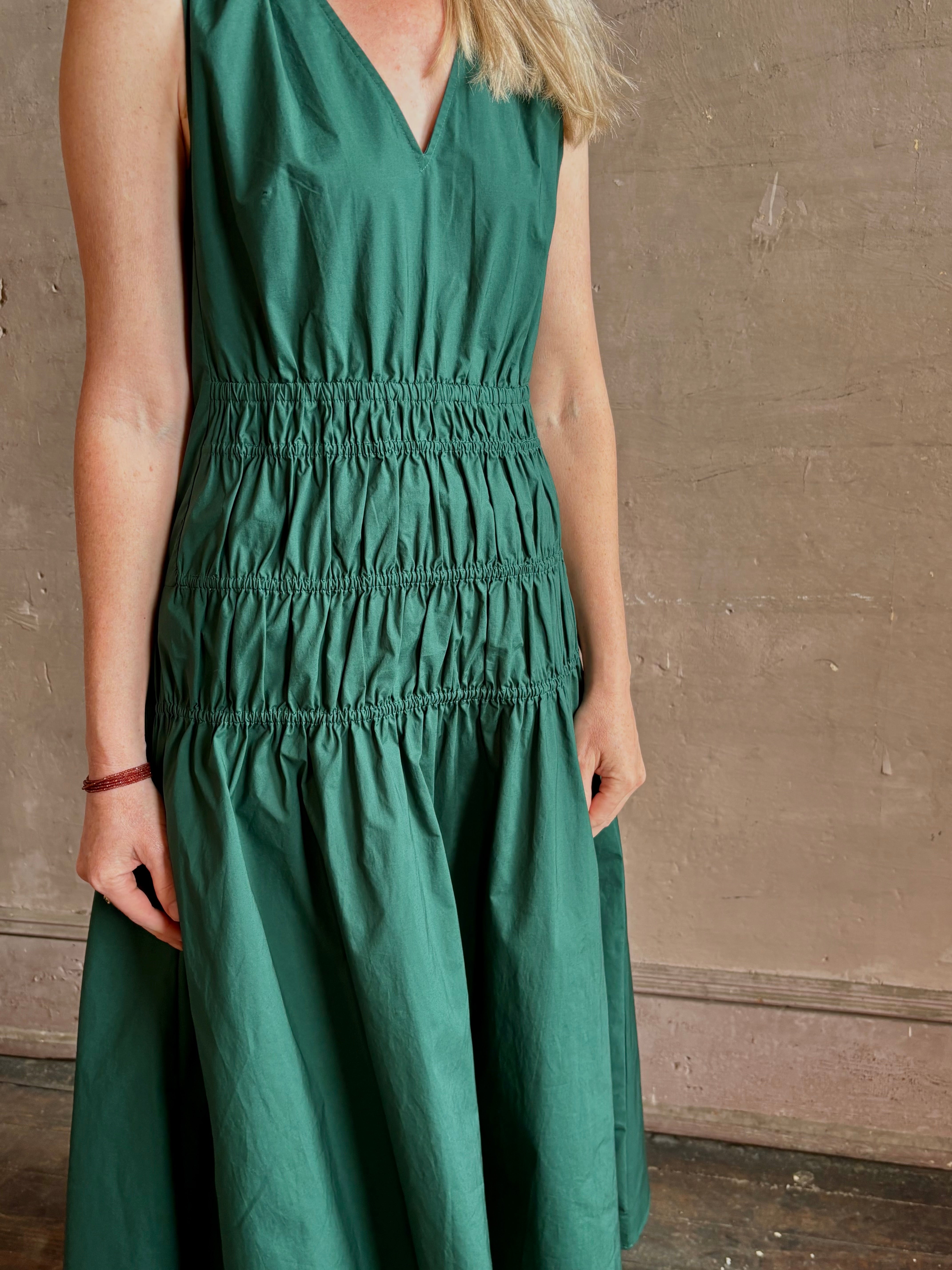 Mature woman wearing Loren Dress from Proenza Schouler White Lable rendered in aspruce green and crafted from a cotton elastane blend with v-neck, sleeveless, pockets, and rushed waist